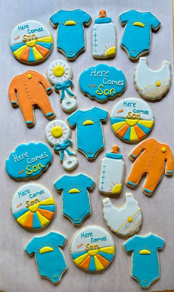 custome sugar cookies for baby shower in colors blue, orange, yellow, gold. Made by Lancaster Lane Treats in Maple Grove, MN with theme "here comes the son".